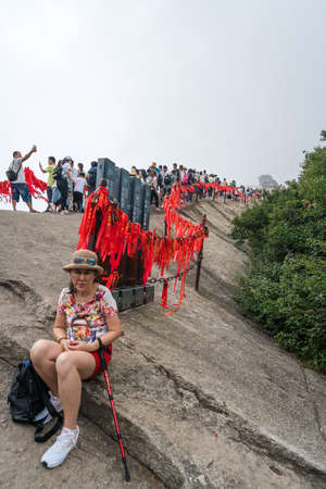 Huashan, China -  August 2019 : Tired chinese woman with a walking pole sitting on a rocky ground and resting on a mountain trail to the West Peak on Huashan mountain, Xian, Shaanxi Provinceのeditorial素材
