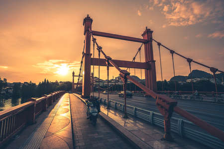 Guilin, China - August 2019 : Man on a motorbike travelling on the Red bridge on Sanduo Lu street at dusk, Guangxi Provinceのeditorial素材