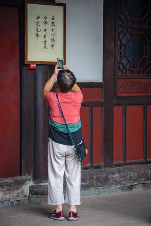 Chengdu, China -  July 2019 :  Chinese woman taking pictures of chinese characters writing displayd on the wall on a temple in the Wenshu Monasteryのeditorial素材