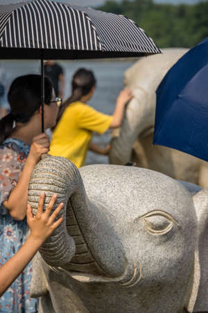 Guilin, China -  August 2019 : Child touching the trunk of the large marble elephant statue next to the landmark Elephant Trunk Hill Arch and the Li River Lijiang River in Guilin, Guangxi Provinceのeditorial素材