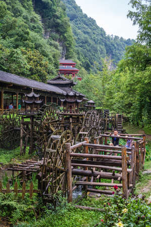 Wulingyuan, China - August 2019 : Man and child using legs to pull levers on a wheel of an old Water wheel in Huanglong Yellow Dragon Cave scenic area, Zhangjiajie, Hunan Provinceのeditorial素材