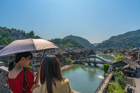 Feng Huang, China -  August 2019 : Women holding umbrella standing on the bridge and admiring the traditional old houses on the riverbanks of Tuo river in Feng huang Old Townのeditorial素材