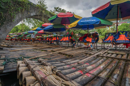 Yangshuo, China -  August 2019 : Small local tourist passenger bamboo boats waiting for people under the historic Yulong Qiao bridge on the shore of scenic Yulong riverのeditorial素材