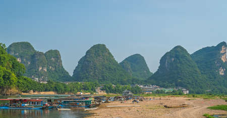 Yangshuo, China - August 2019 : Panoramic view of the OLi river shore with small tourist and fishermen boats on the riverbank, the ferry crossing point in Yangshuo town, Guangxi Provinceのeditorial素材