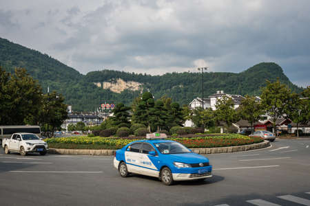 Wulingyuan, China - August 2019 : Taxi leaving the roundabout on a street in the Wullingyuan town, Hunan Province, Chinaのeditorial素材