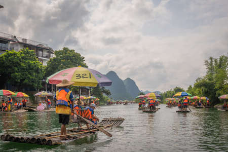 Yangshuo, China -  August 2019 : Small local tourist passenger bamboo boats carrying people on the popular scenic trip along the beautiful scenery of Yulong river in Yangshuoのeditorial素材