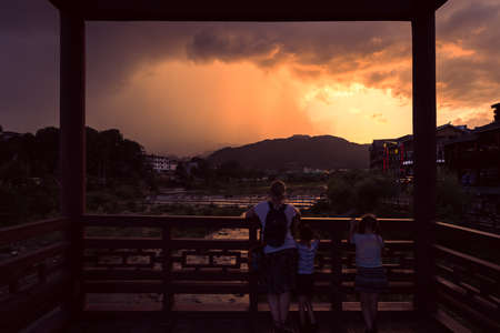 Wulingyuan, China -  August 2019 : Mother with her children standing on the bridge and admiring beautiful sunset over riverのeditorial素材