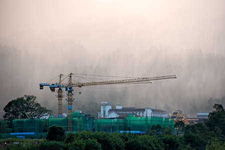 Wulingyuan, China - August 2019 : Cranes on building site in a rain with beautiful rocky karst mountain formations behind in Wulingyuan town, Hunan Provinceのeditorial素材