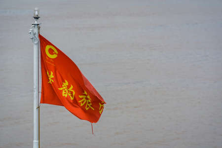 Yangtze River, China - August 2019 : Red and yellow flag with a chinese writing characters on a cruise boat ship sailing on a Yangtzy river in Chinaのeditorial素材