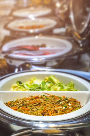 Fried noodles and boiled pakchoy in a serving bowl as a asian style breakfast buffet on the table in...