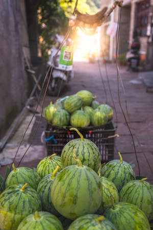 Huge watermelons for sale packed and piled in a plastic boxes to be taken by a porter to the local fruit and vegetable market, Feng Huang town, Chinaの写真素材