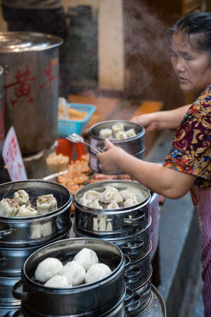 Feng Huang, China - August 2019 : Old woman preparing, cooking and selling delicious traditional chinese dumplings steamed and filled with pork meat, prepared on hot steamのeditorial素材