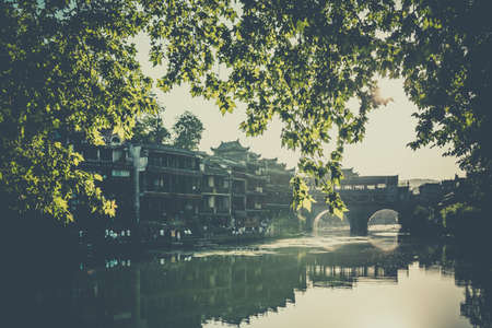 Feng Huang, China -  August 2019 : Morning view of the old historic arched bridge on the riverbanks...
