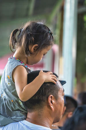 Zhangjiajie, China - August 2019 : Cute little chines girl sitting on her fathers shoulder and looking at smartphone while queuing at the Wullingyuan entrance to the Zhangjiajie national park, Hunan Provinceのeditorial素材