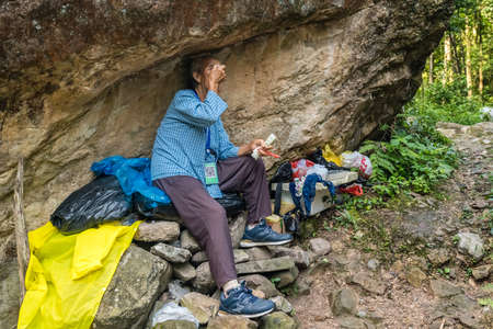 Zhangjiajie, China - August 2019 : Poor old worker woman resting under a huge rocky boulder on a trail in Zhangjiajie National Parkのeditorial素材