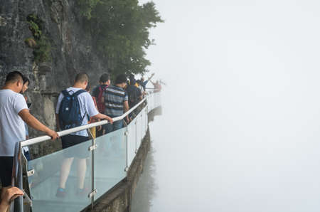 Zhangjiajie, China -  August 2019 : Tourists walking on a narrow glass pathway in Tianmenshan nature parkのeditorial素材