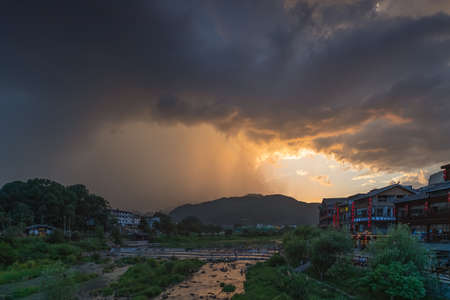 Wulingyuan, China -  August 2019 : People crossing the river during stormy sunset near Xibu Street, located in the ruins of the ancient city of Tujiaのeditorial素材