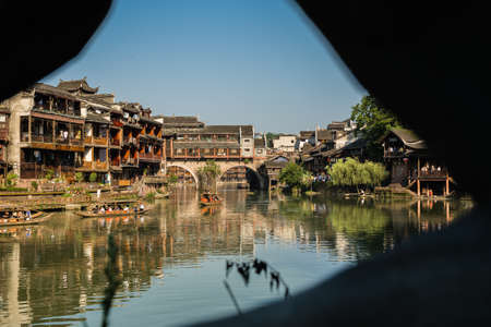 Feng Huang, China -  August 2019 : Group of tourists sailing in old historic wooden boat under the landmark arched bridge on the Tuo river, flowing through the centre of Fenghuang Old Townのeditorial素材
