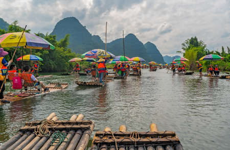 Yangshuo, China -  August 2019 : Tourists sitting on bamboo rafts steered by guides with a long sticks on scenic and beautiful Yulong Riverのeditorial素材