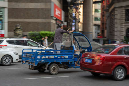 Chongqing, China - August 2019 : Man standing at the back of a small pick up rickshaw driving dangeroulsy fast on the congested street in Chongqingのeditorial素材