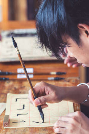 Yangshuo, China - August 2019 : Chinese student holding ink brush during lessons in chinese writing from traditional calligraphy masterのeditorial素材
