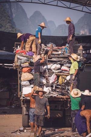 Yangshuo, China - August 2019 : Team group workers people working in a metal recycling courtyard, sorting out pieces of metal and loading it into the back of a large track vehicle, Guangxi Provinceのeditorial素材