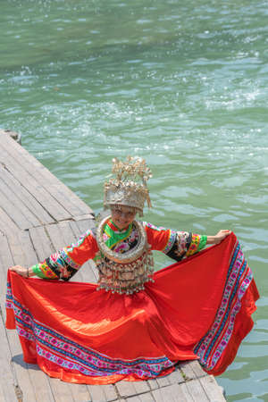 Feng Huang, China -  August 2019 : Beautiful young Chinese woman girl dressed in traditional folk costume and posing for a picture on the wooden path across Tuojiang river in Fenghuang, Hunan Provinceのeditorial素材
