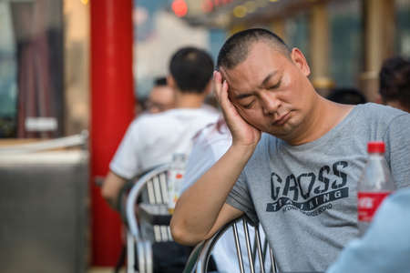 Chongqing, China - August 2019 : Tired chinese male passenger sleeping on a chair boat during trip on a cruise along the mighty Jialing and Yangtze riversのeditorial素材