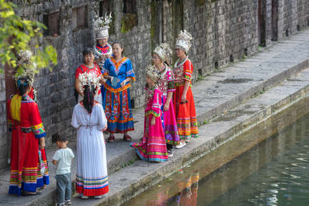 Feng Huang, China -  August 2019 : Group of chinese women dressed in traditional folk costumes standing on the shore riverbank of Tuojiang river in Fenghuang Old Town, Hunan Provinceのeditorial素材