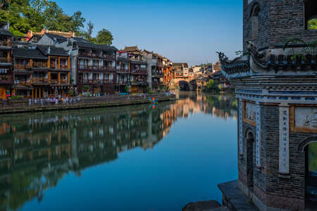 Feng Huang, China -  August 2019 : Water reflection of traditional old wooden houses on the riverbanks of Tuo river, flowing through the centre of Feng huang Old Town on a calm quiet morning in summerのeditorial素材