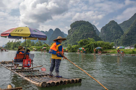 Yangshuo, China - August 2019 : Female guide steering bamboo raft using long stick on the trip on the scenic and beautiful Yulong Riverのeditorial素材