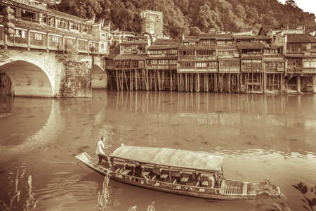 Feng Huang, China -  August 2019 : Sepia vintage view of the old historic wooden tourist boat sailing on the Tuo river, flowing through the centre of Fenghuang Old Townのeditorial素材