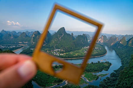 Man holding a frame covering the karst hill landscape as seen from Xianggong Hill viewpoint,...
