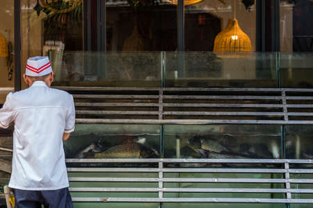 Yangshuo, China - August 2019 : Chef standing outside restaurant serving seafood and looking at the tank storing fresh fishesのeditorial素材