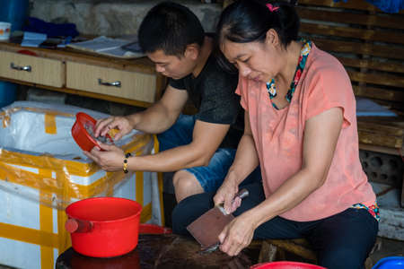 Yangshuo, China - August 2019 : Chinese male and female workers peeling scales off small fish on the street market in Yangshuo, Guangxi Provinceのeditorial素材
