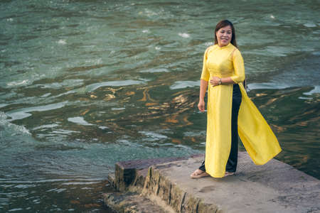 Feng Huang, China -  August 2019 : Beautiful Chinese woman dressed in a yellow silk costume dress posing for a picture on the shore of Tuojiang river in Fenghuang, Hunan Provinceのeditorial素材
