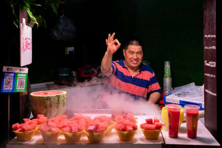 Chongqing, China -  August 2019 :  Happy middle aged chinese man selling portions of freshly cut juicy watermelon  in Ci Qi Kou Old townのeditorial素材
