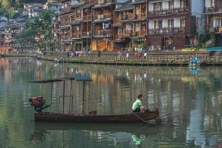 Feng Huang, China - August 2019 : Man sitting at a bow of an old wooden tourist motorboat on the Tuo river, flowing through the centre of Fenghuang Old Townのeditorial素材