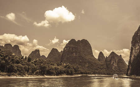 Retro sepia vintage view of the stunning karst mountain scenery on the riverbank of the magnificent Li river near Yangshuo on a hot summer day, Chinaの写真素材