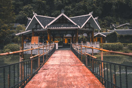 Zhangjiajie, China -  August 2019 : Hanging bridge over small stream leading to the traditional architecture building in Zhangjiajie huanglongdong scenic area, close to the Huanglong Yellow Dragon Caveのeditorial素材