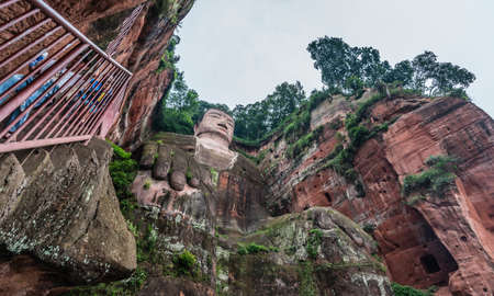 Leshan, China - July 2019 : Crowds of tourists walking down the plank walk around Giant  Leshan Buddha monument, a 71-meter tall stone statue built between 713 and 803 during the Tang Dynasty. Located at the confluence of the Minjiang, Dadu and Qingyi rivのeditorial素材