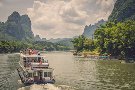 Yangshuo, China - August 2019 : Chinese women standing on the top viewing deck of a sightseeing boat during  journey  on the magnificent Li river from Guilin to Yangshuoのeditorial素材