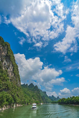 Yangshuo, China - August 2019 : Vertical image of sightseeing boat carrying tourists sailing among stunning karst mountain scenery on the magnificent Li river between Guilin and Yangshuo townsのeditorial素材