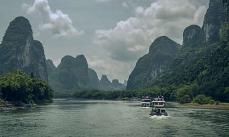 Yangshuo, China - August 2019 : Sightseeing boat carrying tourists sailing among stunning karst mountain scenery on the magnificent Li river between Guilin and Yangshuo townsのeditorial素材