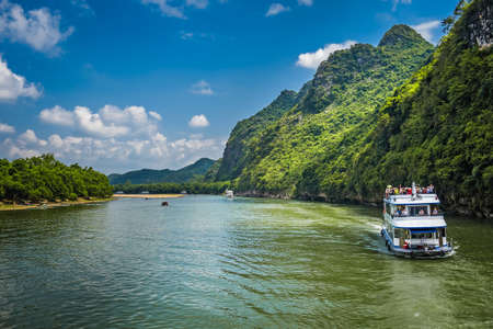 Yangshuo, China - August 2019 : Sightseeing boat carrying tourists sailing among stunning karst mountain scenery on the magnificent Li river between Guilin and Yangshuo townsのeditorial素材