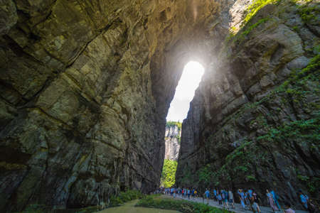 Wulong, China - August 2019 : Crowds of tourists walking on a narrow path towards the natural rocky...