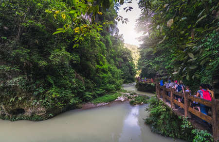 Wulong, China - August 2019 : Tourists walking on a wooden artificial bridge path along a river flowing through the landscape of the massive vertical rock walls in Wulong National Parkのeditorial素材