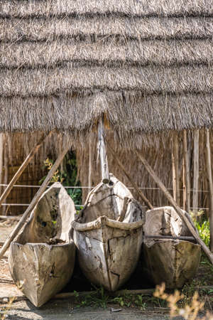 Traditional wooden fishing pirogues stored on the ground under village hut with straw roofの写真素材