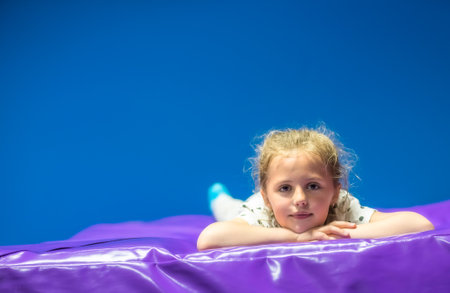 Cute Caucasian girl resting on a soft mat after jumping in the trampoline center, children playgroundの写真素材