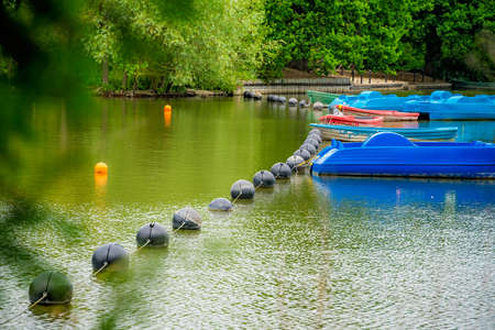 View of a small boating lake pond with a row of paddle boats parked, Crystal Palace Park, London,...